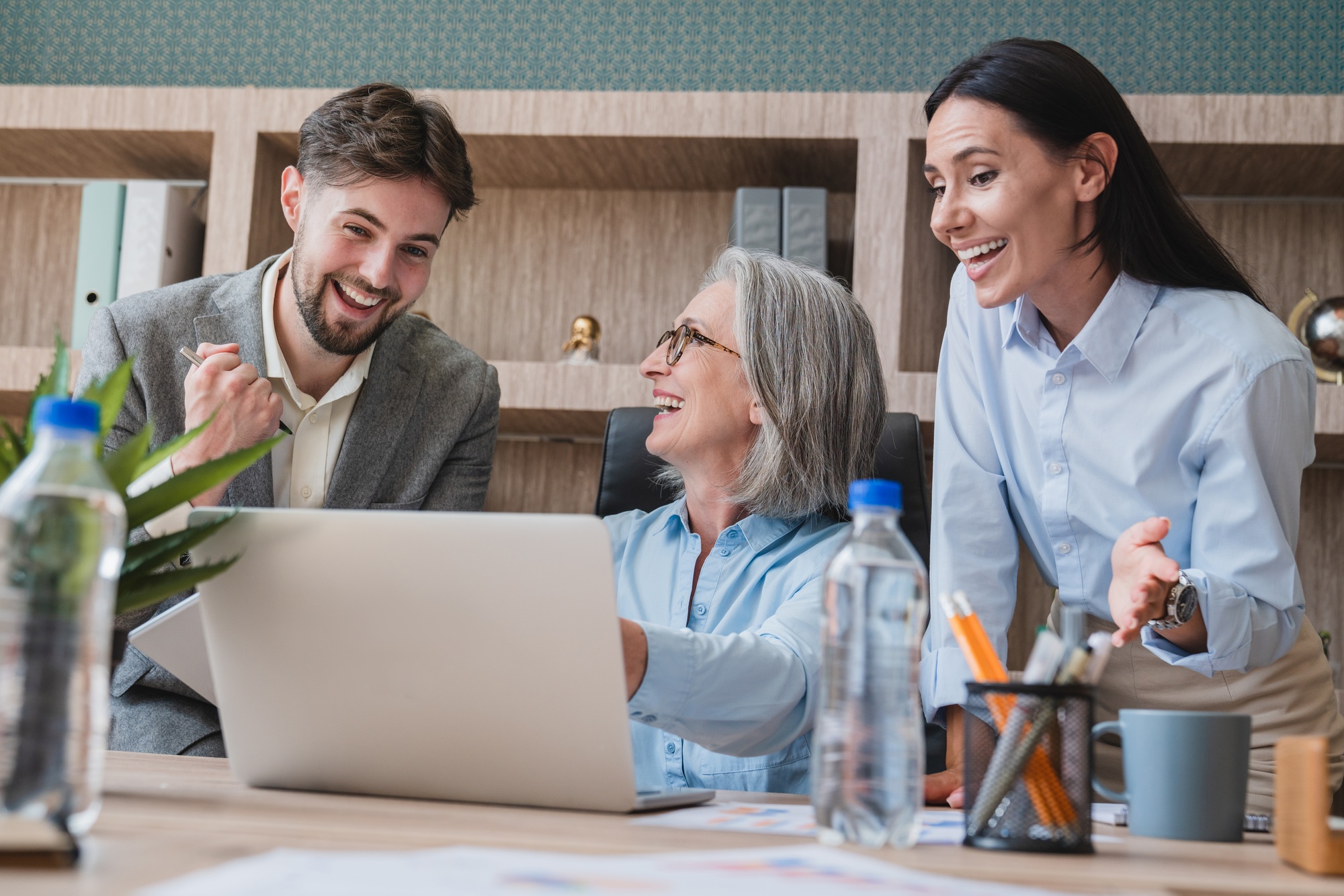 Professional Team Collaborating Enthusiastically Around a Laptop in a Modern Office Setting